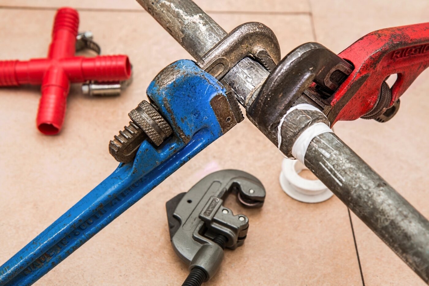 Pipe wrenches and a length of copper pipe on a tiled floor